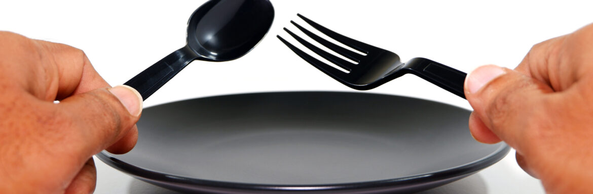 Cutlery set holding hand before black plate with white background close-up view