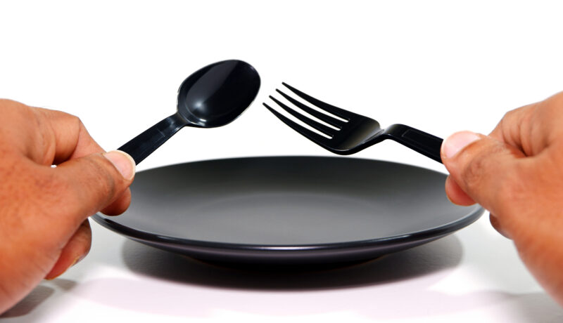 Cutlery set holding hand before black plate with white background close-up view